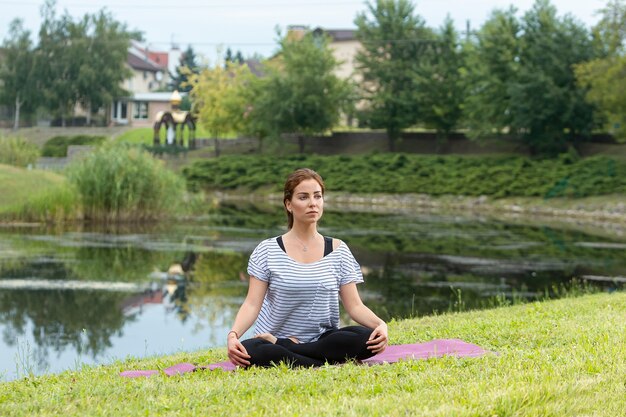 Giovane bella donna che fa esercizio di yoga nel parco verde. Stile di vita sano e concetto di fitness.