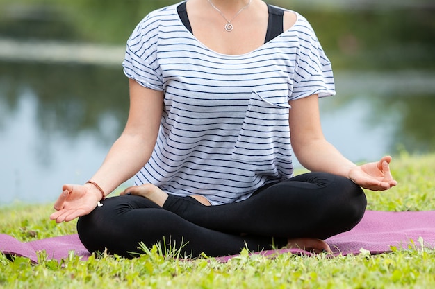 Giovane bella donna che fa esercizio di yoga nel parco verde. Stile di vita sano e concetto di fitness.