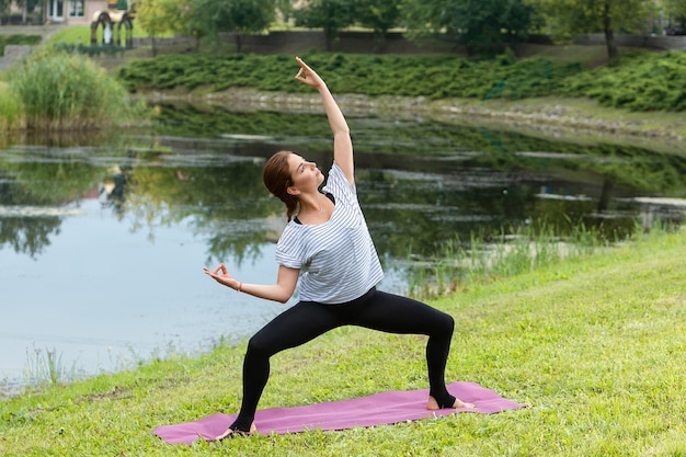 Giovane bella donna che fa esercizio di yoga nel parco verde