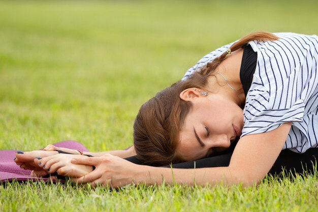 Giovane bella donna che fa esercizio di yoga nel parco verde