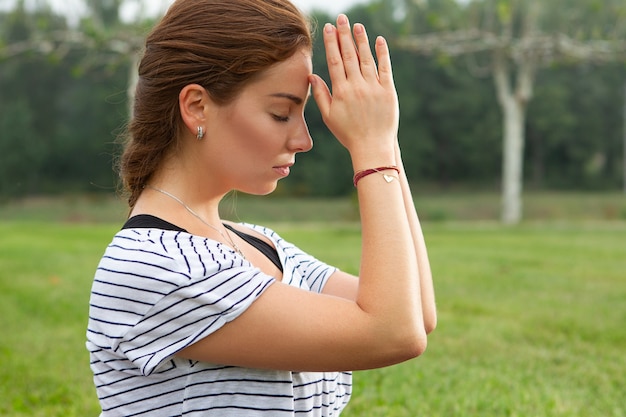 Giovane bella donna che fa esercizio di yoga nel parco verde