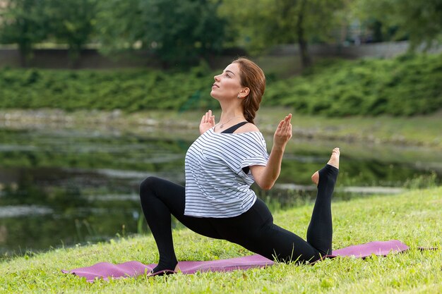 Giovane bella donna che fa esercizio di yoga nel parco verde