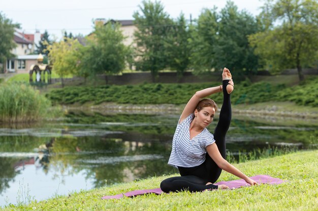 Giovane bella donna che fa esercizio di yoga nel parco verde