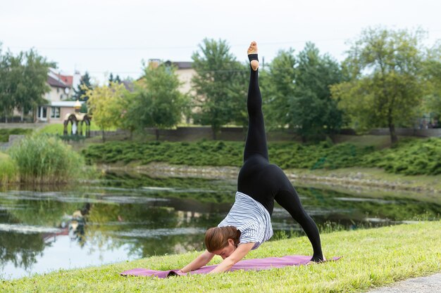 Giovane bella donna che fa esercizio di yoga nel parco verde