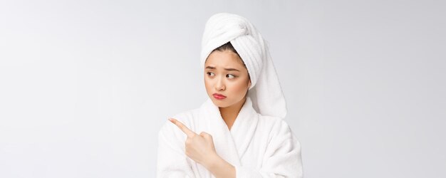 Giovane bella donna che indossa asciugamano doccia dopo il bagno su sfondo bianco isolato che punta con il dito