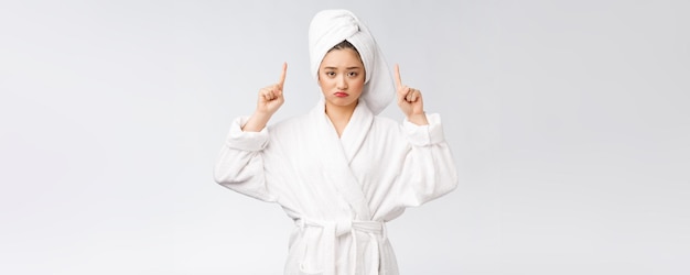 Giovane bella donna che indossa asciugamano doccia dopo il bagno su sfondo bianco isolato che punta con il dito
