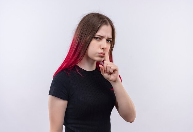 giovane bella donna che indossa la maglietta nera che mostra il gesto di silenzio sul muro bianco isolato