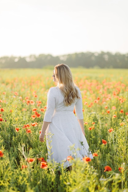 Giovane bella donna che indossa un abito bianco in posa in un campo di papaveri