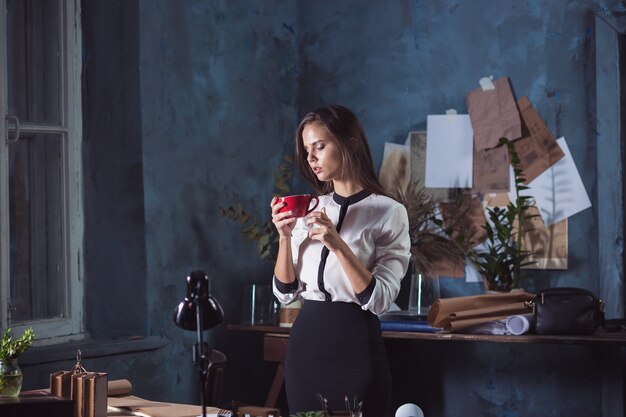 Giovane bella donna che lavora con una tazza di caffè e un taccuino in ufficio loft
