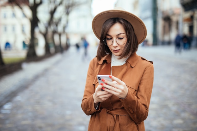 Giovane bella donna che manda un sms sulla via di autunno dello smartphone