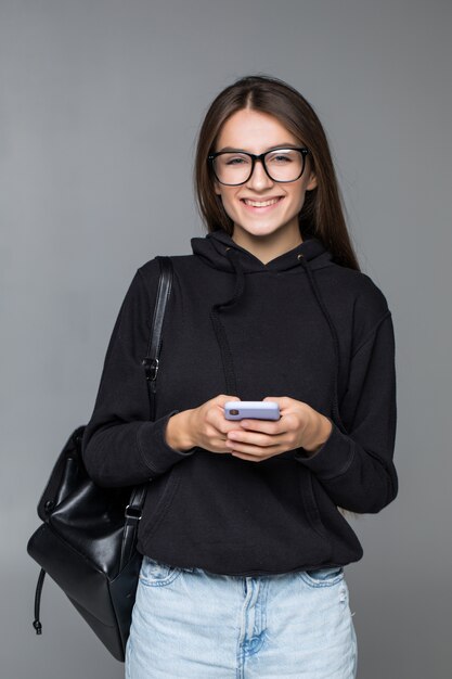 Giovane bella donna che per mezzo dello Smart Phone isolato sulla parete grigia