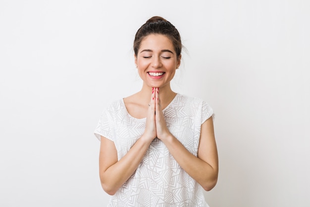 Giovane bella donna che prega con un sorriso, esprimendo un desiderio, gli occhi chiusi,