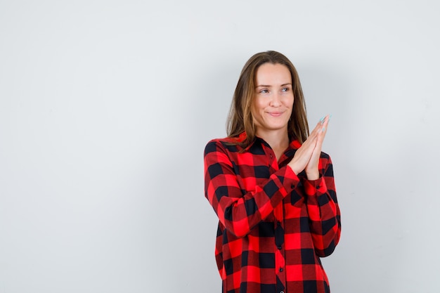 Giovane bella donna che preme le mani insieme in camicia casual e sembra allegra, vista frontale.