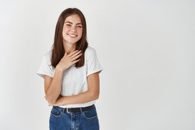 Giovane bella donna che riceve lodi e sorride, in piedi felice sul muro bianco.