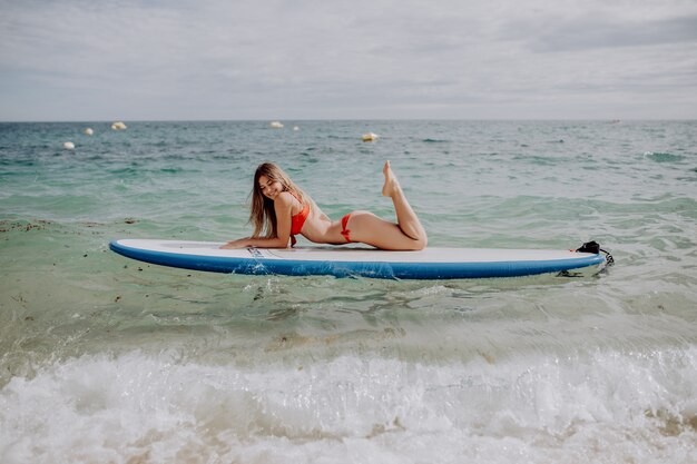 Giovane bella donna che si distende nel mare su una tavola di SUP.