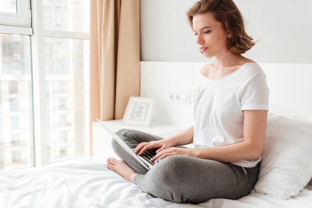 Giovane bella donna che si siede all'interno per mezzo del computer portatile