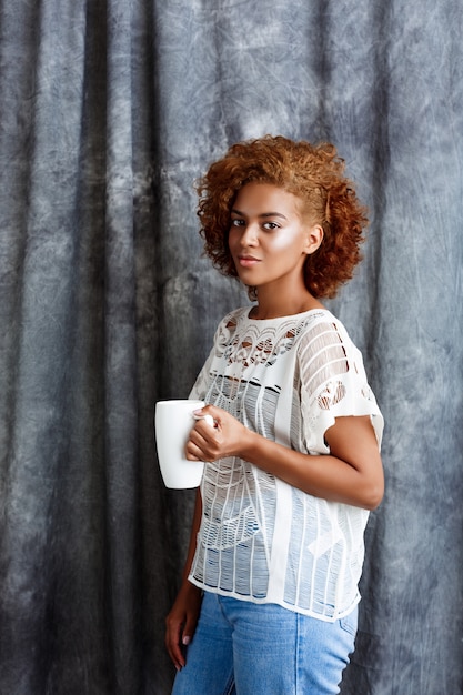 Giovane bella donna che tiene tazza, in posa