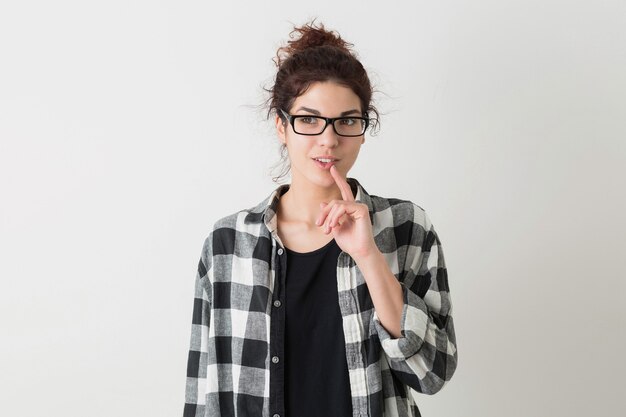 Giovane bella donna con gli occhiali pensando, avendo un'idea, sorridente, felice, sincera emozione, espressione del viso, isolato su sfondo bianco, camicia a scacchi, stile hipster, studente, tenendo il dito sulle labbra