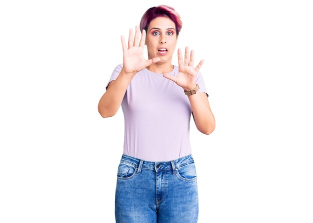 Giovane bella donna con i capelli rosa che indossa abiti casual impauriti e terrorizzati con il gesto di arresto dell'espressione di paura con le mani che gridano nel concetto di shock panico