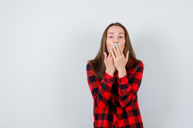 Giovane bella donna con le mani sulla bocca in camicia casual e dall'aspetto allegro. vista frontale.