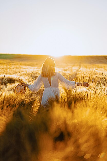 giovane bella donna con lunghi capelli biondi in un vestito bianco su un campo di grano al mattino presto all'alba. L'estate è tempo di sognatori, capelli svolazzanti, una donna che corre attraverso il campo sotto i raggi