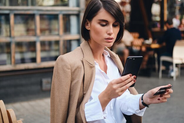 Giovane bella donna d'affari alla moda con carta di credito che utilizza con sicurezza il cellulare nella caffetteria sulla strada