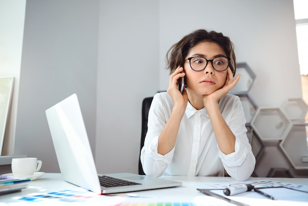 Giovane bella donna di affari che parla sul telefono nel luogo di lavoro in ufficio. Distogliere lo sguardo