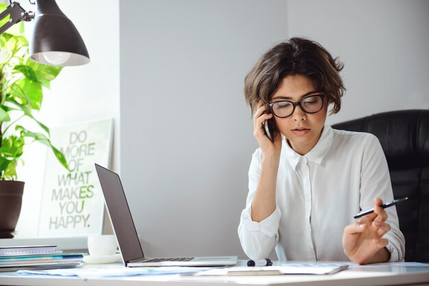 Giovane bella donna di affari che parla sul telefono nel luogo di lavoro in ufficio.