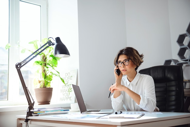 Giovane bella donna di affari che parla sul telefono nel luogo di lavoro in ufficio.