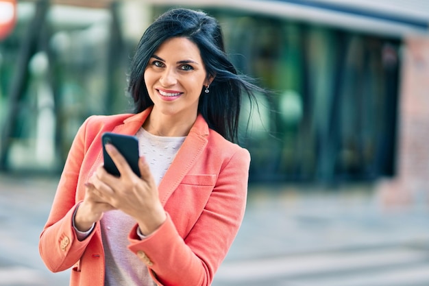 Giovane bella donna di affari che sorride felice facendo uso dello smartphone alla città