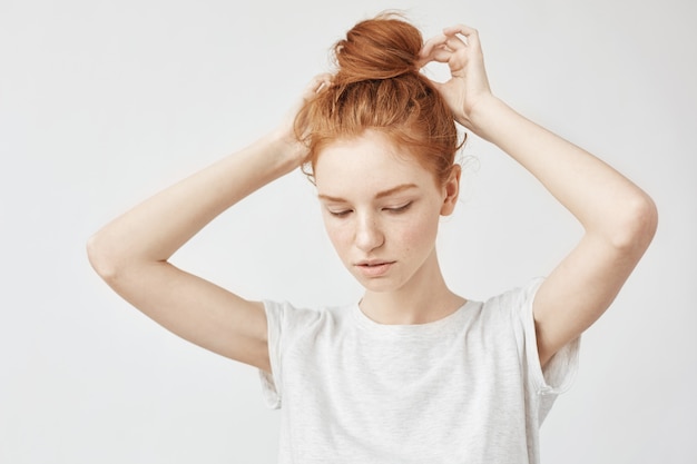 Giovane bella donna di redhead che corregge il panino dei capelli.