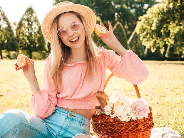 Giovane bella donna hipster in jeans estivi alla moda, maglietta rosa e cappello. Donna che fa picnic all'esterno.