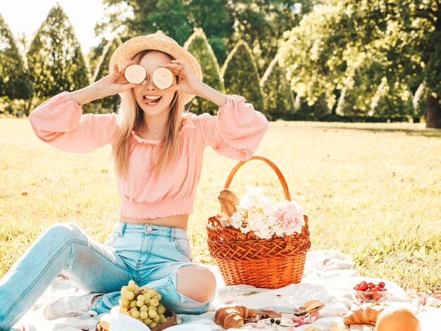 Giovane bella donna hipster in jeans estivi alla moda, maglietta rosa e cappello. Donna che fa picnic all'esterno.