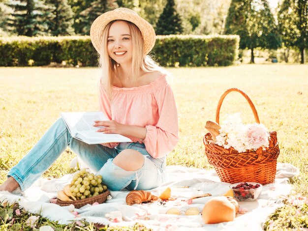 Giovane bella donna hipster in jeans estivi alla moda, maglietta rosa e cappello. Donna spensierata che fa picnic all'esterno.