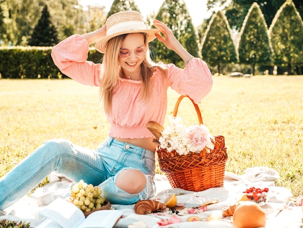 Giovane bella donna hipster in jeans estivi alla moda, maglietta rosa e cappello. Donna spensierata che fa picnic all'esterno.