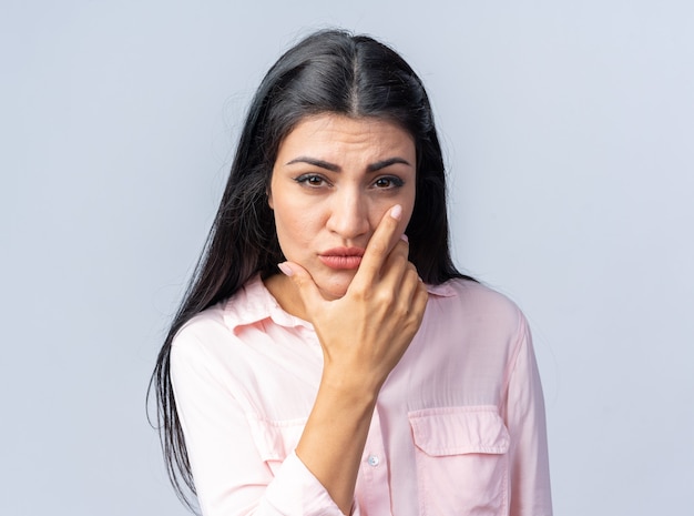 Giovane bella donna in abiti casual che guarda con la mano sul mento pensando con faccia seria