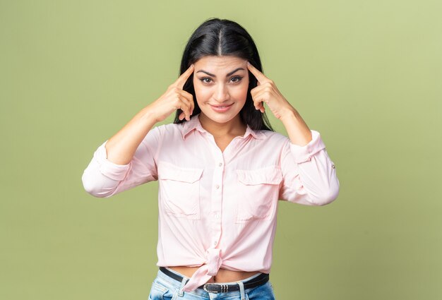 Giovane bella donna in abiti casual che sembra sorridente fiduciosa che punta con l'indice alle tempie