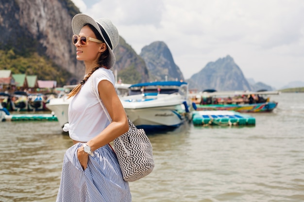 Giovane bella donna in abito di moda estiva, stile casual, in viaggio con zaino, cappello, occhiali da sole, vacanze in thailandia, asia