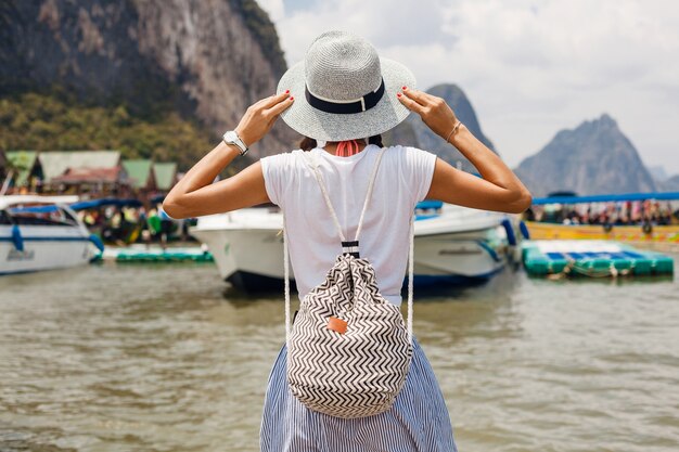 Giovane bella donna in abito di moda estiva, stile casual, in viaggio con zaino, cappello, occhiali da sole, vacanze in thailandia, asia