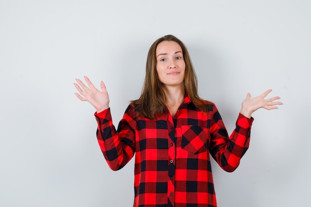 Giovane bella donna in camicia casual che mostra gesto impotente e guardando beata, vista frontale.