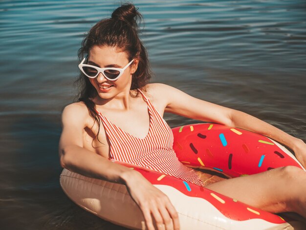 Giovane bella donna in costume da bagno e occhiali da sole galleggianti sul mare