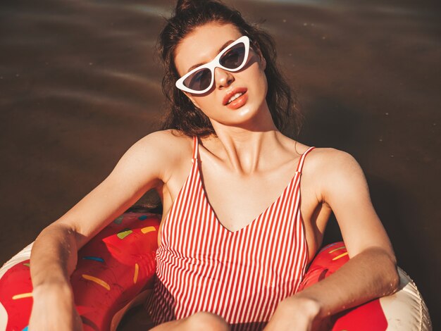 Giovane bella donna in costume da bagno e occhiali da sole galleggianti sul mare