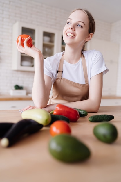 Giovane bella donna in cucina in un grembiule e verdure fresche sul tavolo