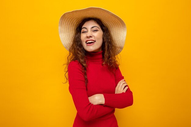 Giovane bella donna in dolcevita rosso in cappello estivo che sembra felice e allegro sorridente ampiamente