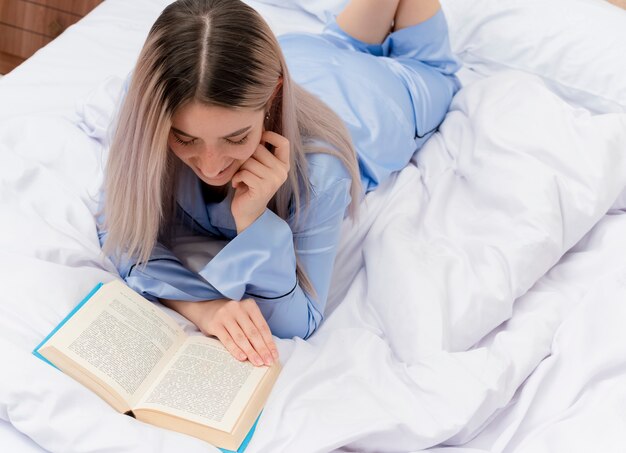 Giovane bella donna in pigiama blu che pone sul letto