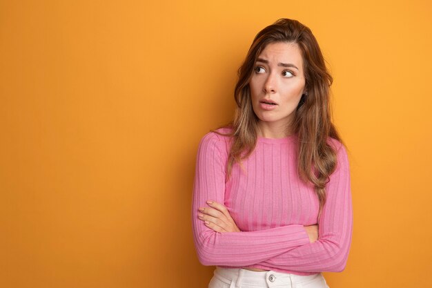 Giovane bella donna in top rosa che guarda da parte preoccupata e confusa in piedi sopra l'arancia