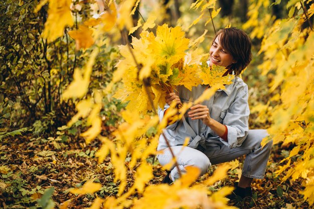 Giovane bella donna in un parco in autunno pieno di foglie