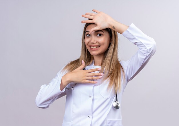 Giovane bella donna medico indossa camice bianco con lo stetoscopio che sembra confuso facendo gesto di difesa con le palme aperte