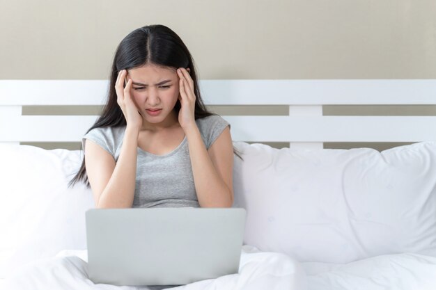 Giovane bella donna seduta sul letto, lei usa il computer portatile si sente serio e mal di testa