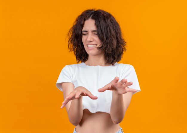 Giovane bella donna sorridente che allunga le mani con gli occhi chiusi sulla parete arancione isolata con lo spazio della copia